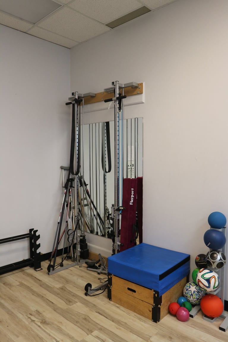 Pilates reformer machine in studio with exercise balls, foam roller, and wooden storage box on wooden floor