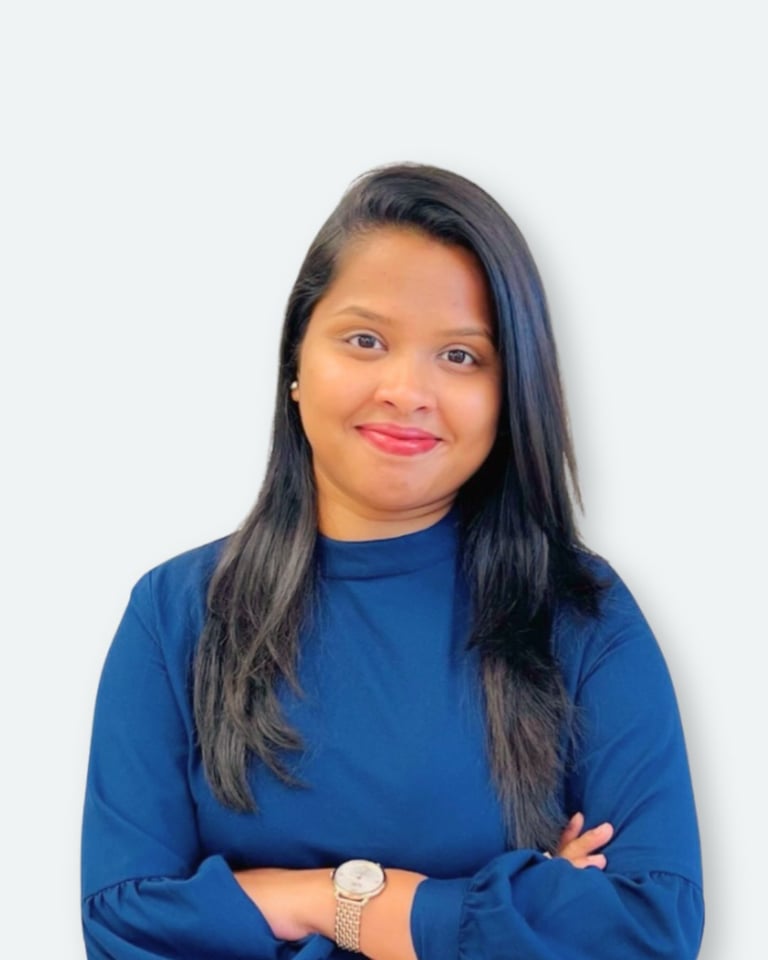 Woman with long dark hair wearing a blue top and watch, smiling at camera with arms crossed against white background