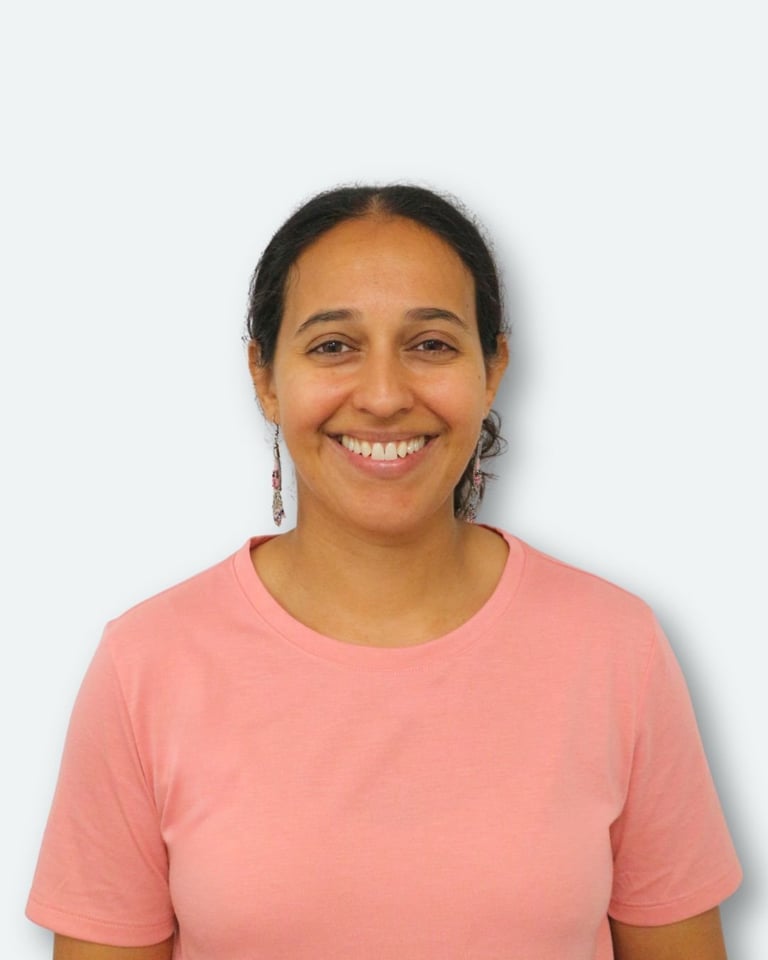 Smiling woman with dark hair pulled back, wearing a pink t-shirt and dangling earrings against a white background