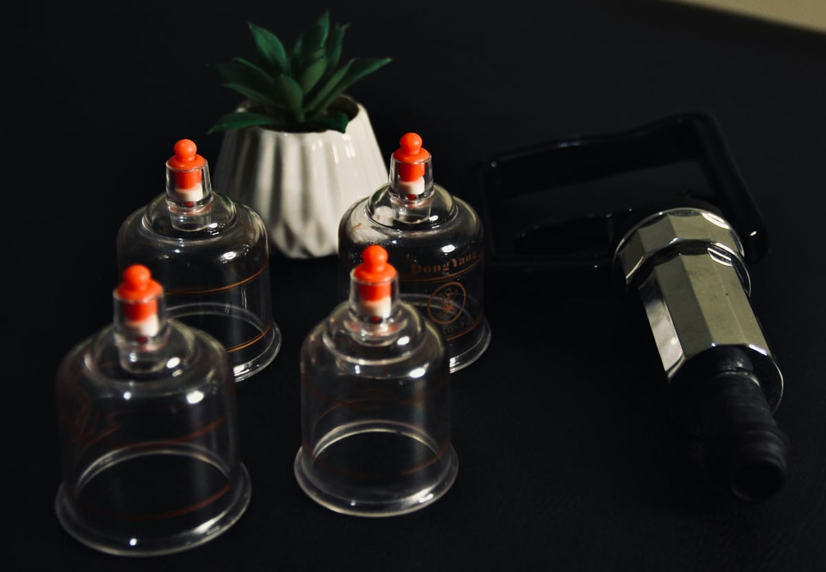 Four glass cupping therapy cups with orange bulbs beside a pump, with a potted succulent in the background