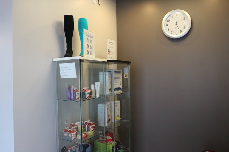 Glass display cabinet with shelves containing products, wall clock above, and items on top including bottles and boxes