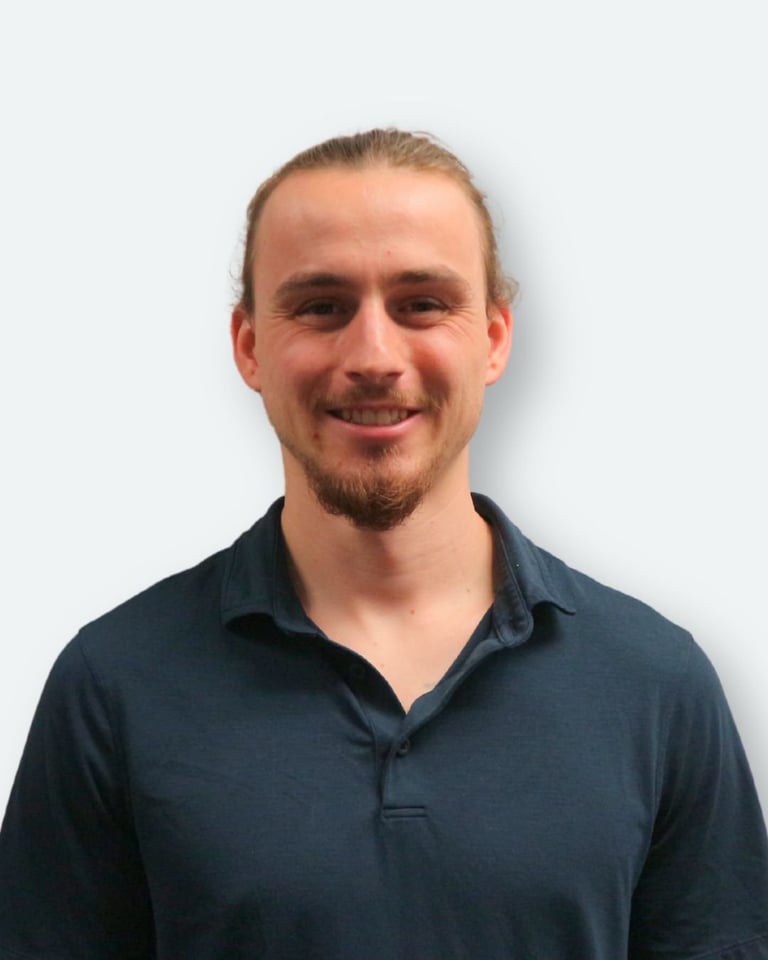 Headshot of a smiling man with blonde hair and facial hair wearing a dark blue polo shirt against a white background