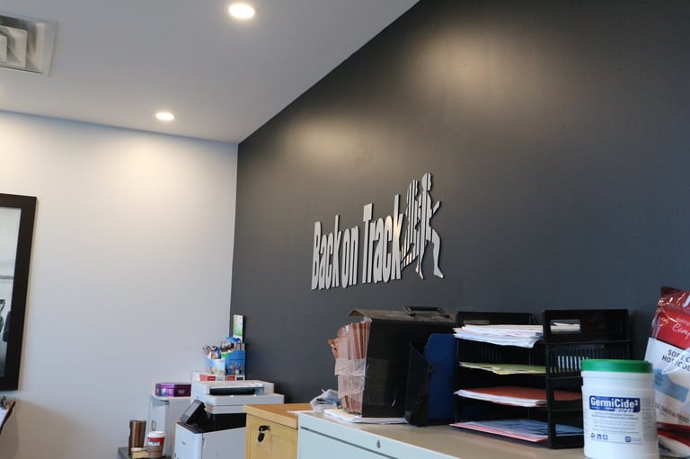 Modern office reception desk with white counter, dark gray accent wall, illuminated white signage, and organized supplies.