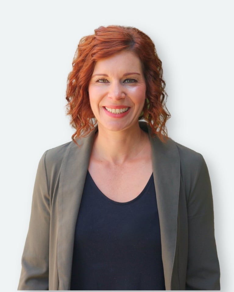 Professional headshot of a woman with red curly hair wearing a gray cardigan over a dark navy top, smiling at the camera against a white background