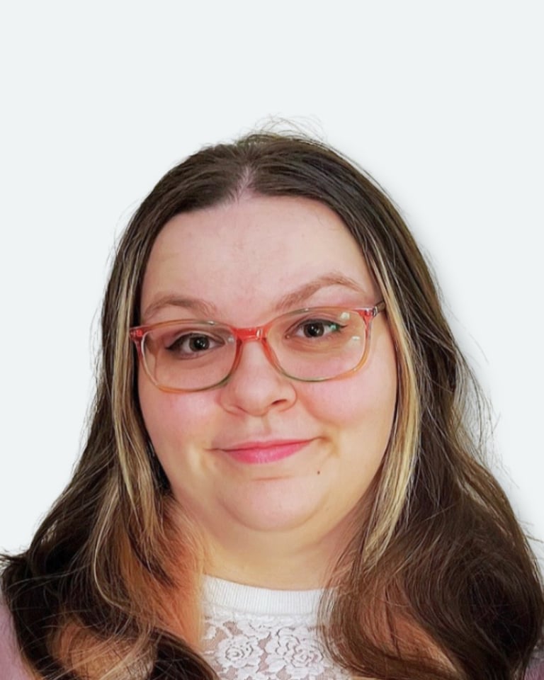 Portrait of a woman with long brown hair, wearing coral-pink glasses and a light-colored top, smiling at the camera against a white background