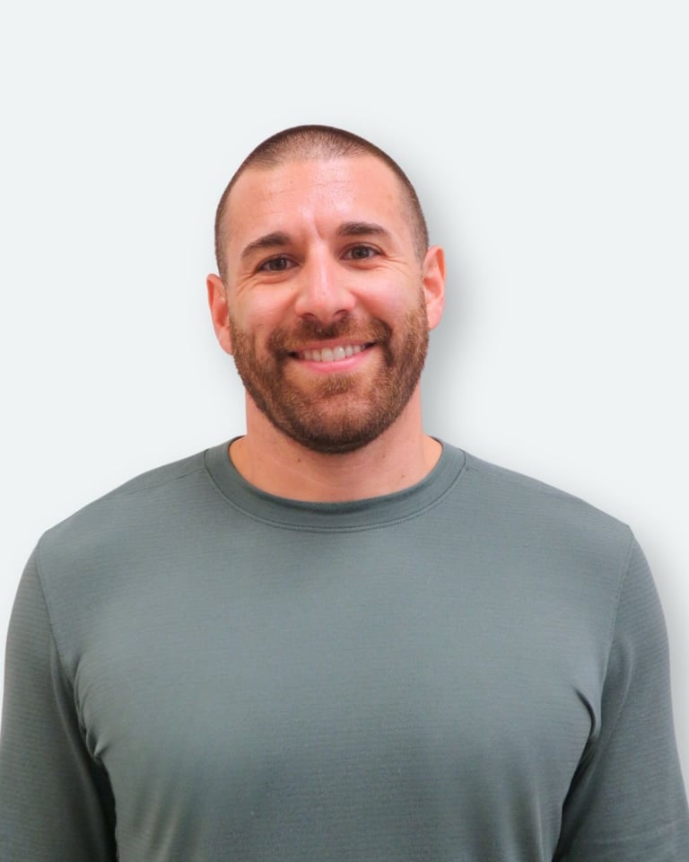Portrait of a smiling man with short hair and beard wearing a gray crew neck shirt against a white background
