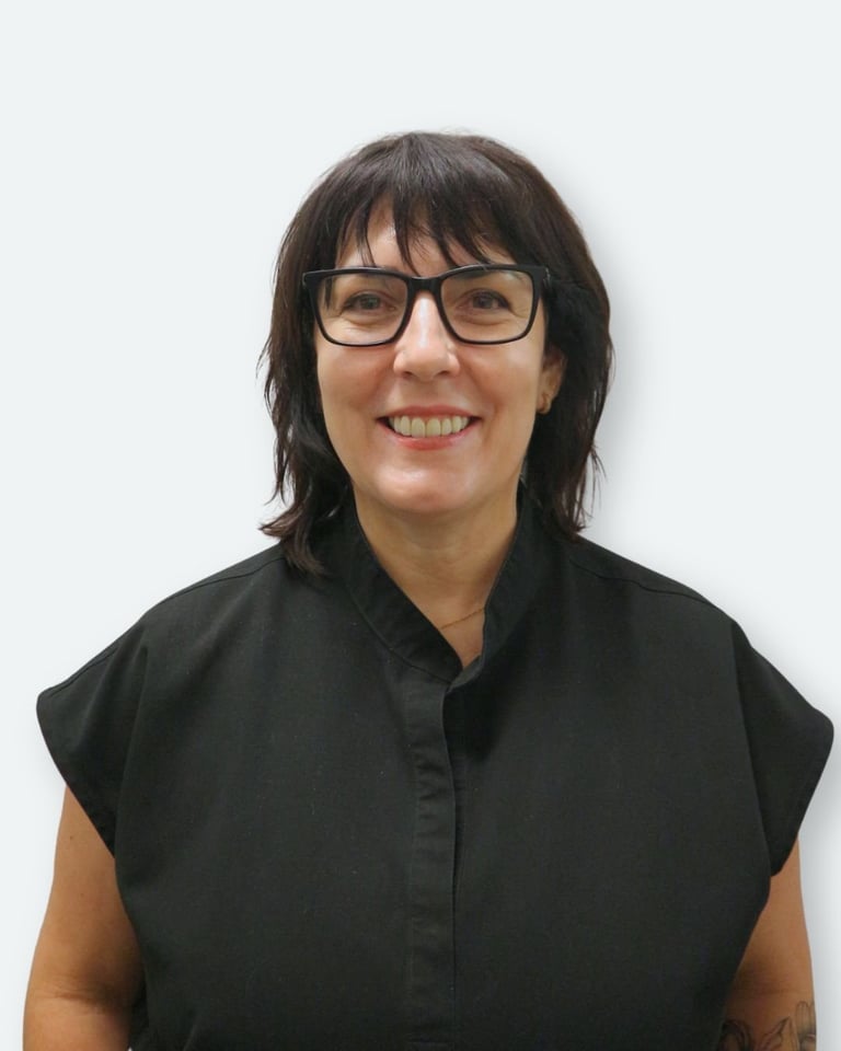 Portrait of a woman with dark shoulder-length hair and glasses, wearing a black sleeveless shirt, smiling at the camera against a white background
