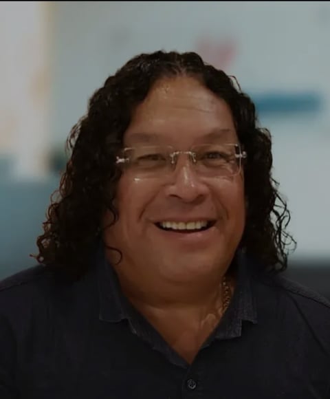 Portrait of a smiling man with long dark curly hair and glasses wearing a dark shirt