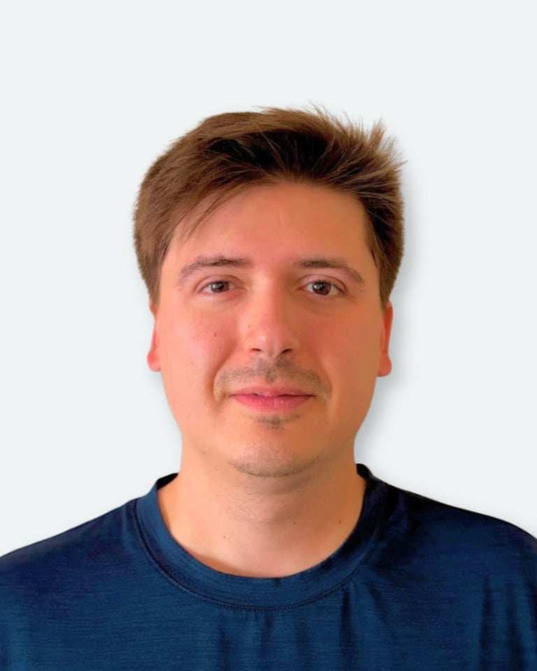 Portrait photo of a man with brown hair wearing a dark blue t-shirt against a light background