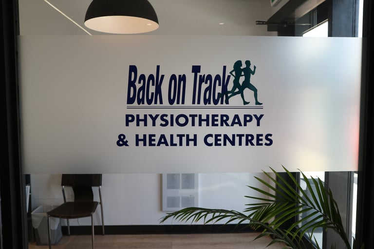 Back on Track Physiotherapy and Health Centres logo on white wall in modern clinic reception area with black pendant light and potted plant