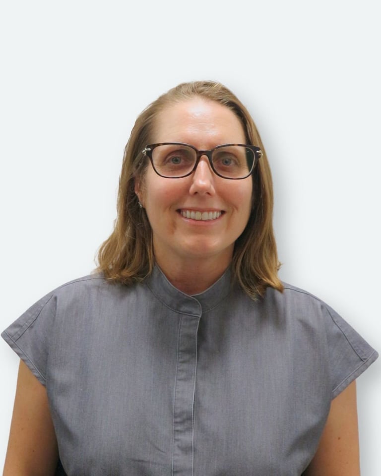Headshot of smiling woman wearing glasses and gray button-up shirt against white background