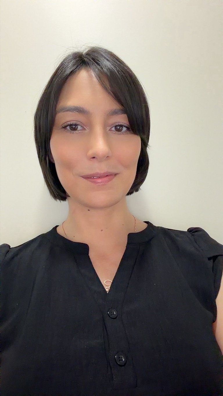 Portrait of a woman with dark shoulder-length hair wearing a black sleeveless button-up shirt against a neutral background