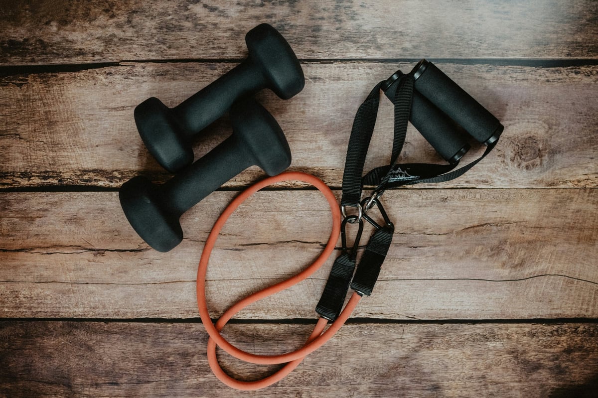 Fitness equipment including black dumbbells and a red resistance band with handles on wooden surface