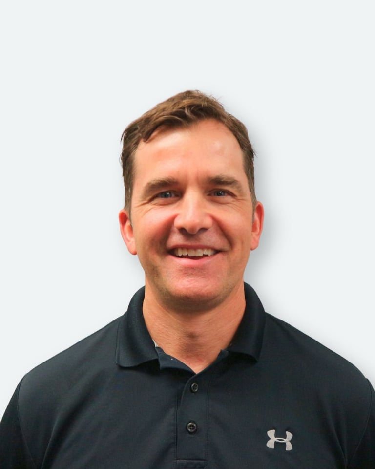 Smiling man with brown hair wearing a black Under Armour polo shirt against a white background