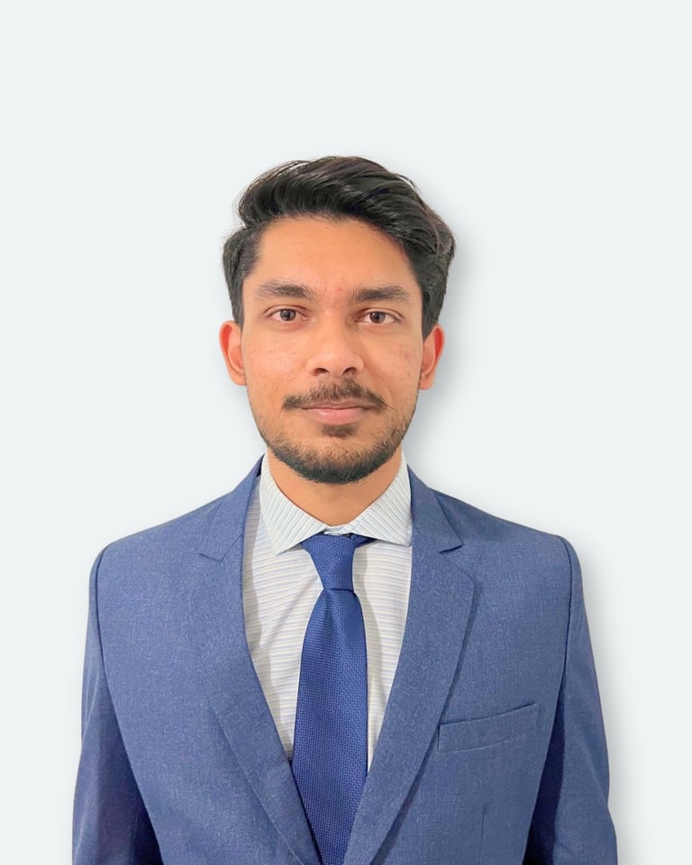 Professional headshot of a man with dark hair and facial hair wearing a blue blazer, striped shirt, and dark blue tie against a white background