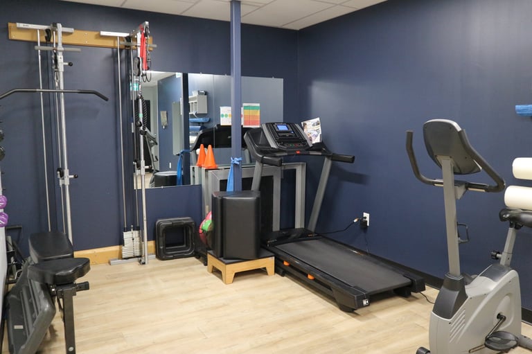 Modern gym interior with cardio equipment including treadmill, stationary bike, and weight machines against dark blue walls