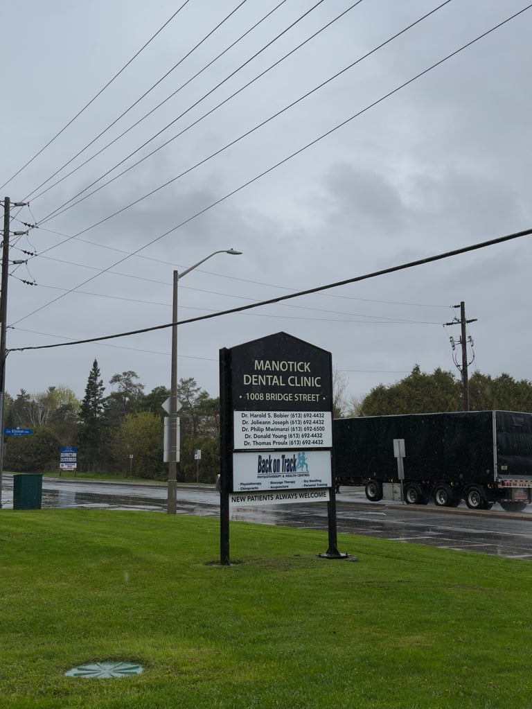 Manotick Dental Clinic sign on grassy area with utility poles and overcast sky