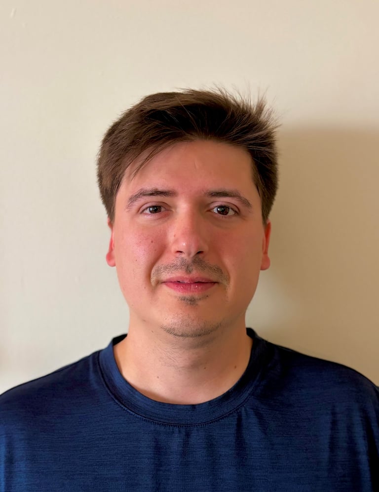 Headshot of a man with dark hair and mustache wearing a navy blue t-shirt against a neutral background