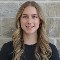 Portrait of a young woman with long blonde wavy hair wearing a black shirt against a brick wall