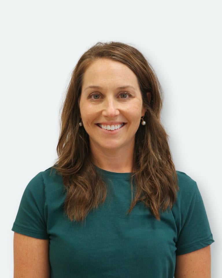 Portrait of a smiling woman with long brown hair wearing a dark teal t-shirt against a white background