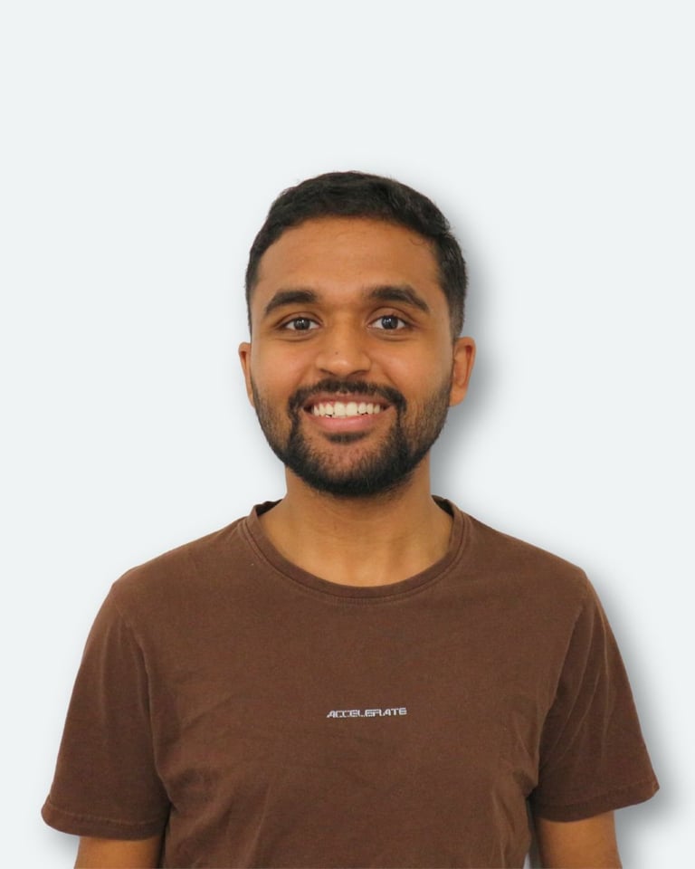 Portrait of a smiling man with dark hair and beard wearing a brown t-shirt against a white background